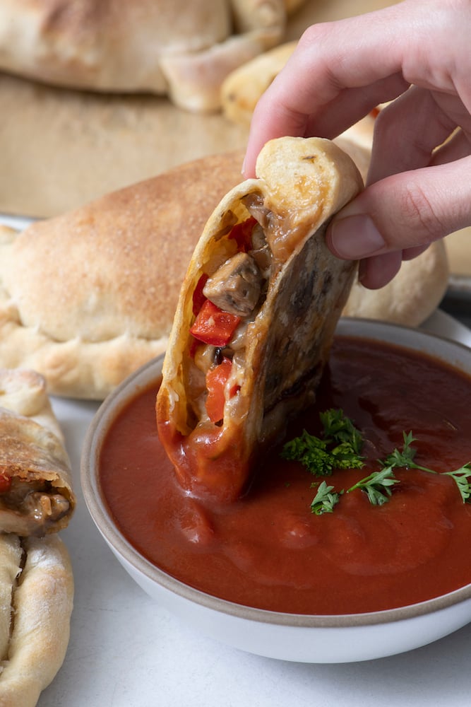 Hand dipping Vegetarian Calzone into pizza sauce.