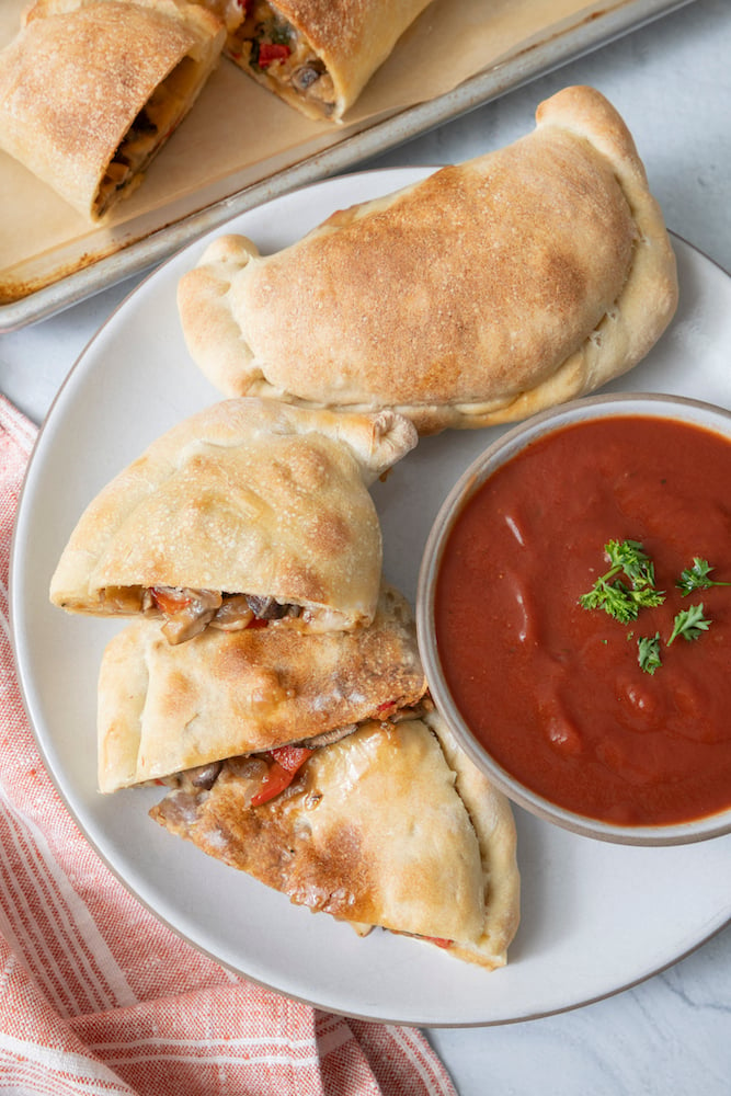 Vegetarian Calzones on a plate with pizza sauce in a bowl on the side. 